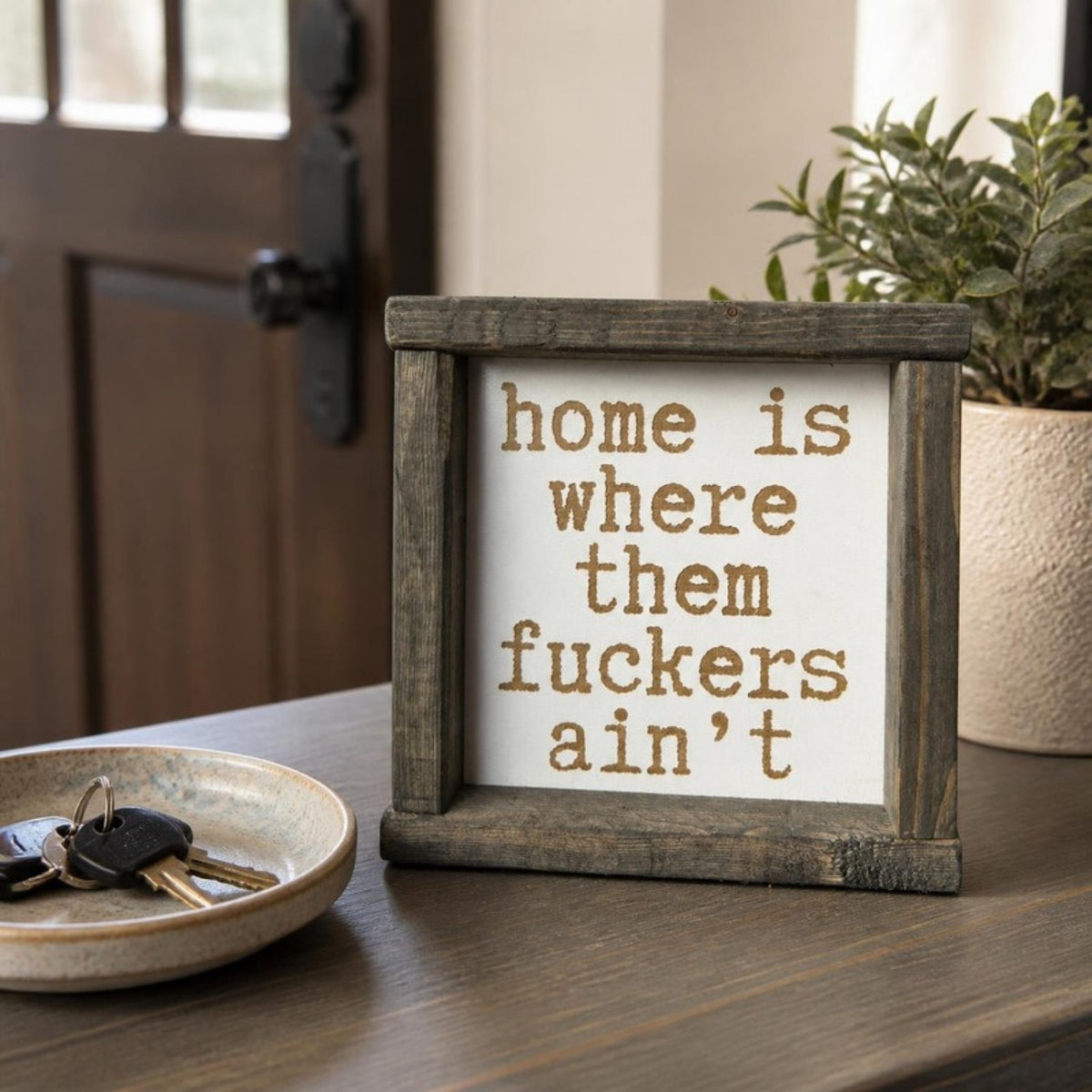Home is where those fuckers ain't framed sign on an entryway table
